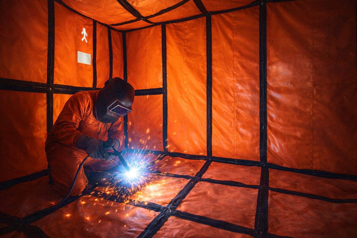 Worker welding inside a pressurized welding habitat system for safe hot work in hazardous industrial environments
