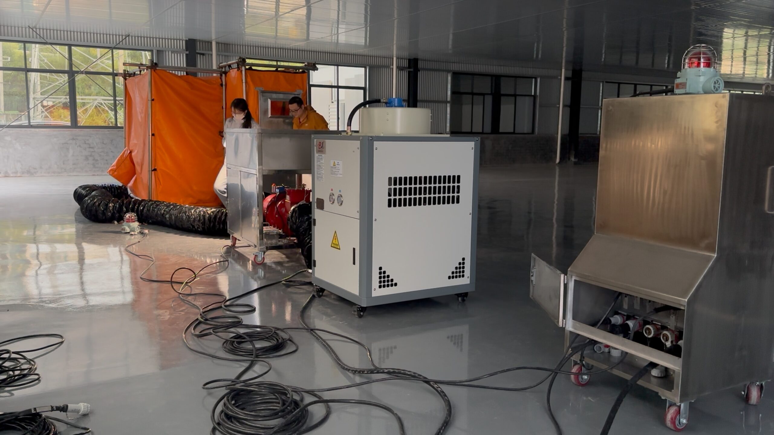 Industrial welding habitat system setup in a factory workshop, featuring an orange fireproof enclosure, ventilation ducts, control equipment, and safety testing devices.