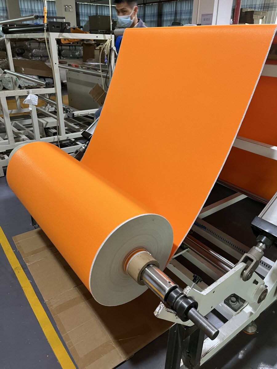 Orange silicone coated fiberglass fabric roll being processed on a production machine for welding habitat panels and fire-resistant industrial enclosures.