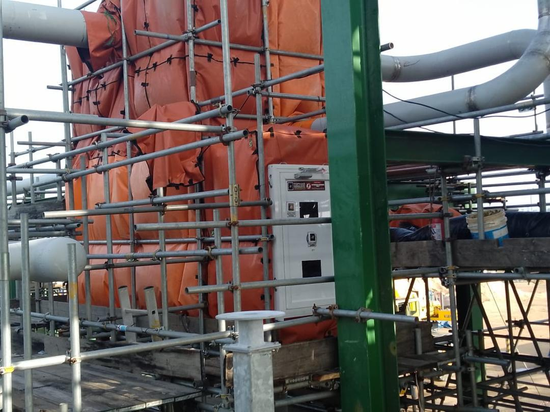 Orange fire-resistant welding habitat enclosure installed on an industrial scaffold structure for hot work safety, pipe maintenance, and worker protection in a plant environment.